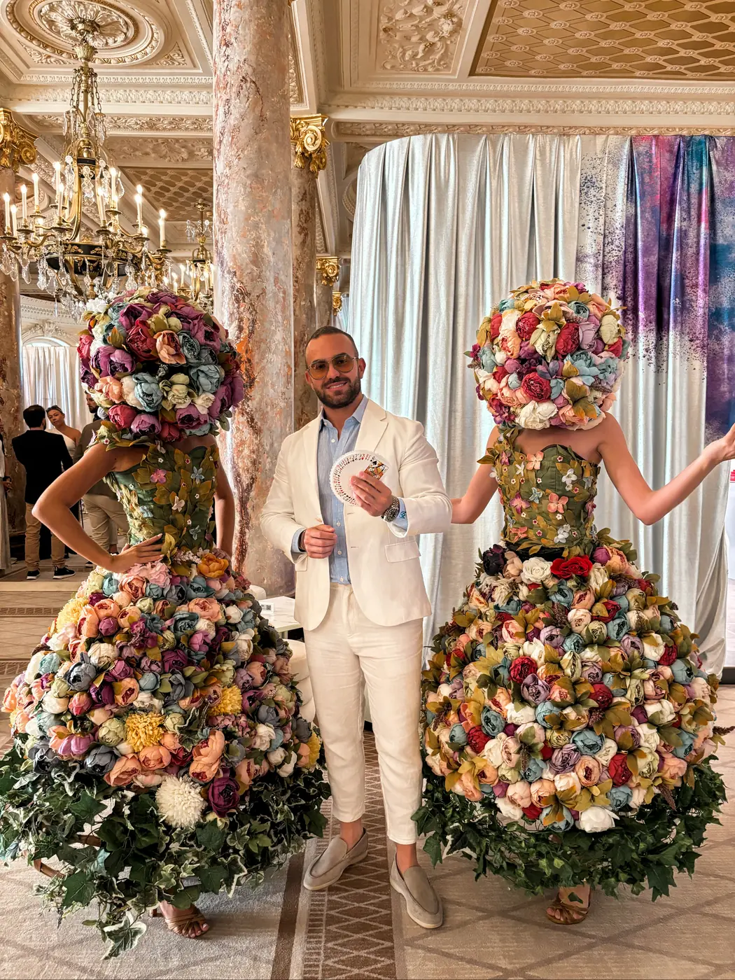 Matteo Cammisa fanning a deck of cards between two floral-gown performers in the gilded ballroom of the Carlton Cannes