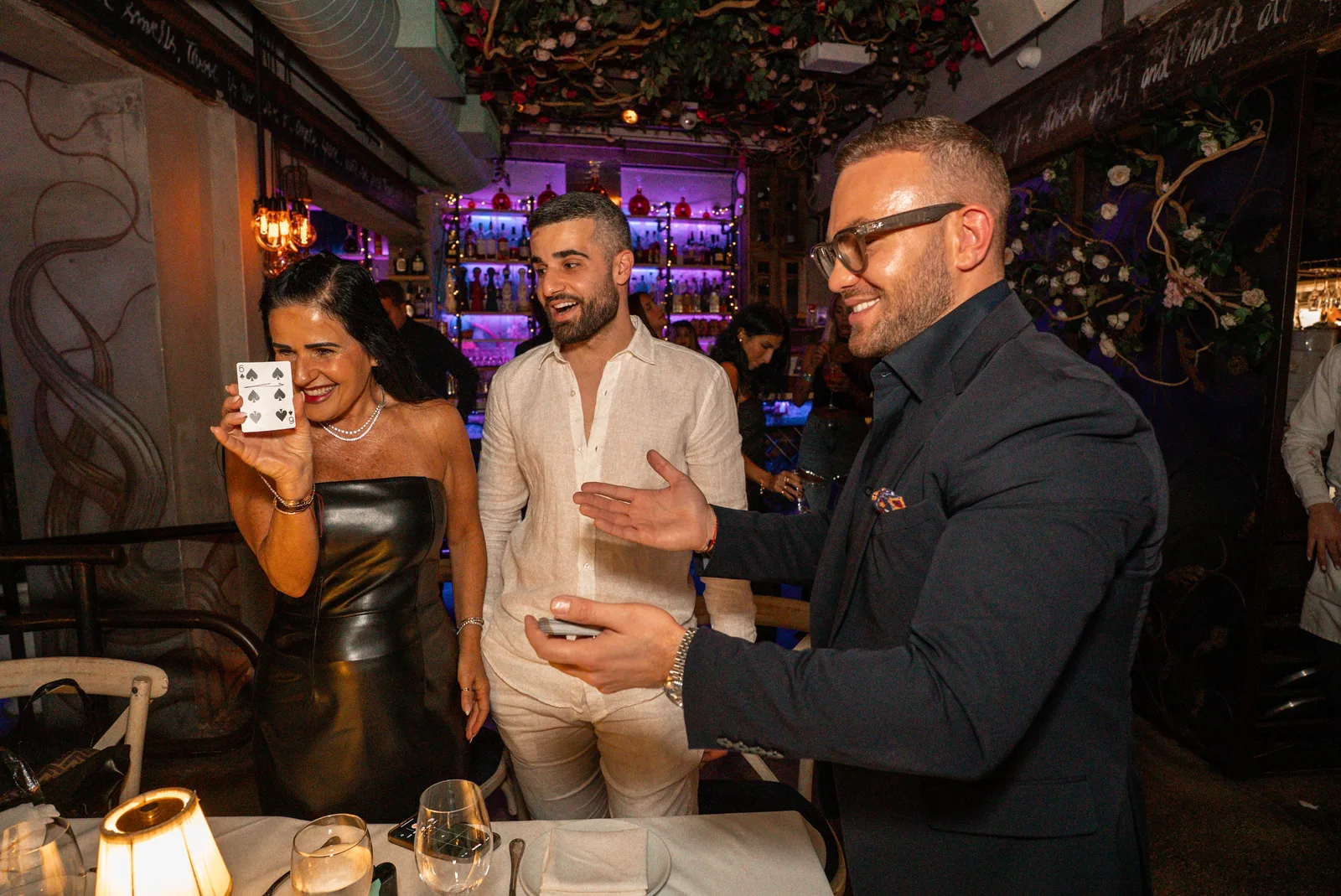 Matteo Cammisa performing a card effect tableside at Kiki on the River, Miami — a guest holding up the six of spades, the room laughing
